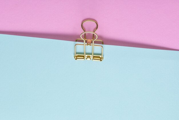 Photo golden paper clip and  paper sheets on blue and pink background