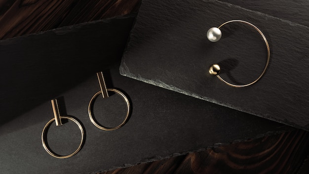 Golden pearl bracelet and golden earrings pair on stone trays on dark wood