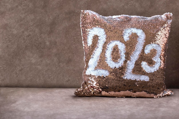 Golden pillow with paillettes on the brown sofa with inscription 2023. Pillow with sequins