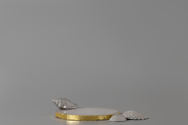 Golden podium with silver seashells on the gray background. Podium for product, cosmetic presentation. Creative mock up. Pedestal or platform for beauty products.