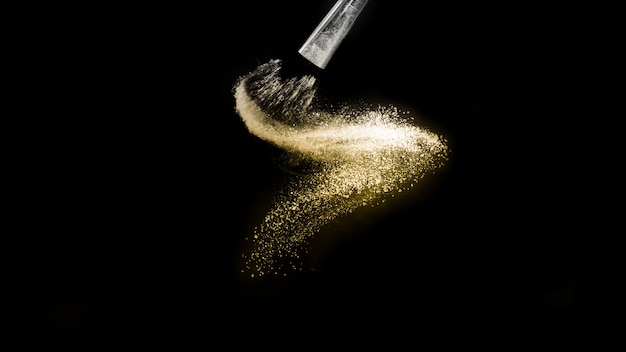 Golden powder splash and brush for makeup artist or beauty blogger in black background