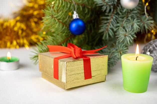 Golden present gift box with red ribbon next to the christmas tree, candles and holiday decoration.