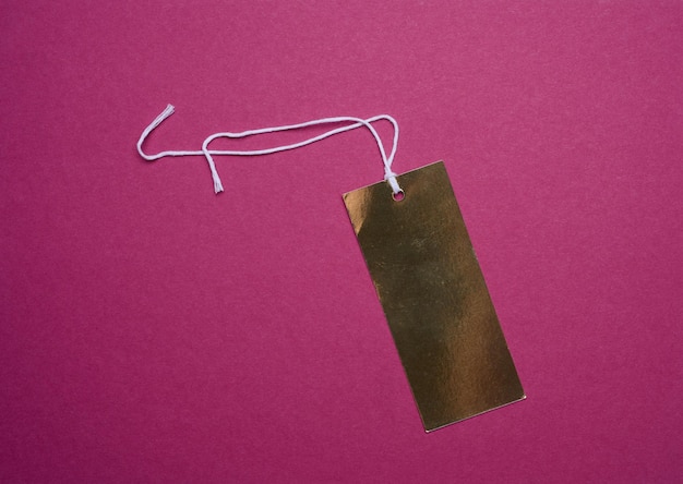 Golden price tag with a white string for clothing and merchandise on a pink background