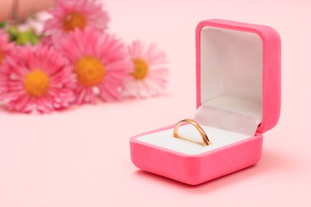 Golden ring in a box and flowers on a pink background. Women jewelry and accessories.