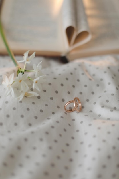 Golden ring and open book with folded sheets in heart shape in\
bed