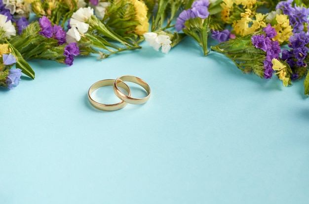 Golden rings with colored flowers on blue surface, wedding template.