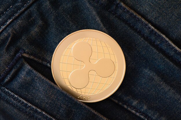 A golden ripple cryptocurrency coin protrudes from the pocket of blue frayed jeans virtual money