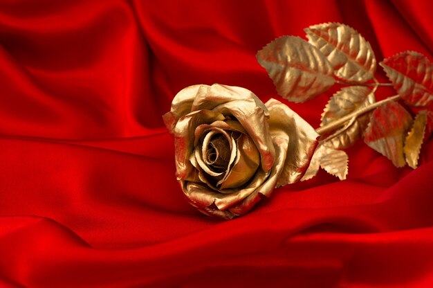 Фото Золотой цветок розы на гладком красном атласном фоне