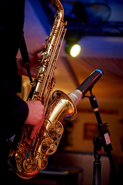 A golden saxophone in the hands of a musician near the microphone on the counter.