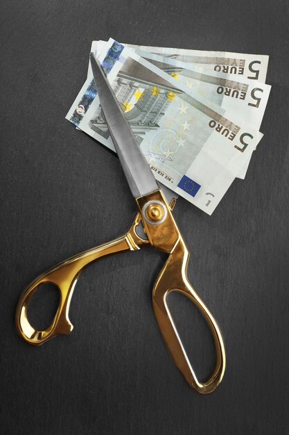 Golden scissors cut money on black background