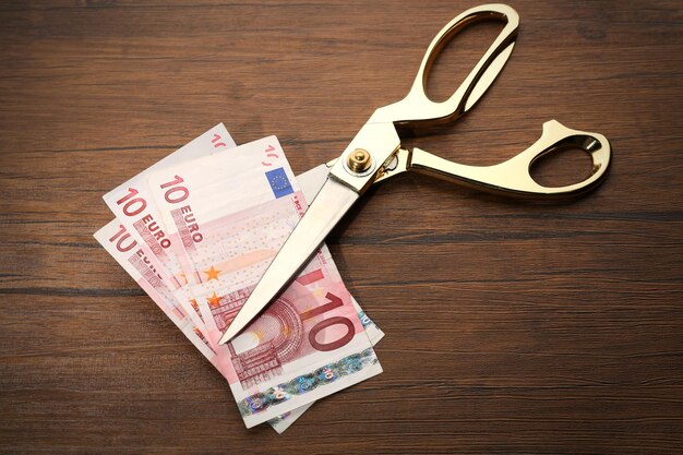 Golden scissors cut money on wooden background