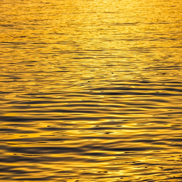 夕焼けの黄金の海の波が表面の背景として輝きます。夏休みと沿岸の自然の概念