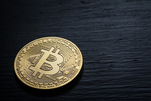 Golden shiny bitcoin on a black wooden wall