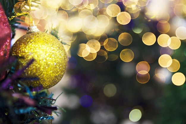 Golden shiny glittering ball on Christmas tree with blurred lights. Holiday concept. Close up.