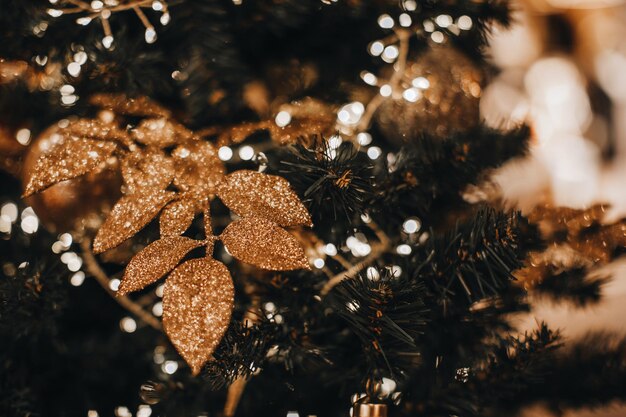 Golden shiny leaves hanging on the Christmas tree Magic bokeh lights festive garlands Fairy winter