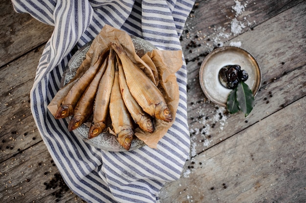 Golden smoke-dried fish on plate on a baking paper on the grey striped napkin on the wooden table.