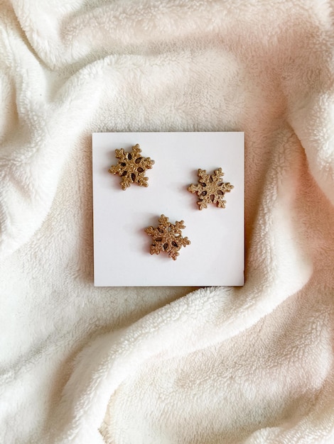 Golden snowflakes lie on a white square on a white furry fluffy background View from above Flatlay