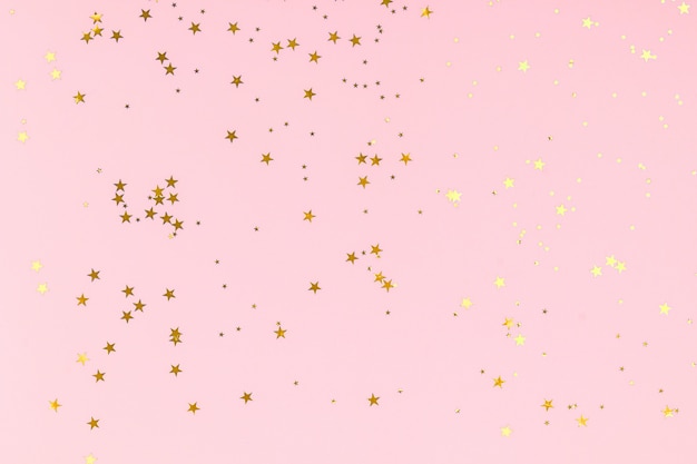 Golden stars glitter confetti in abstract style on pink background. Gold sparkles texture. Holiday new year backdrop. Anniversary, birthday. Greeting card template.