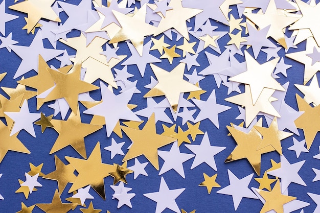 Golden stars and white confetty on blue background selective focus Festive holiday pastel backdrop