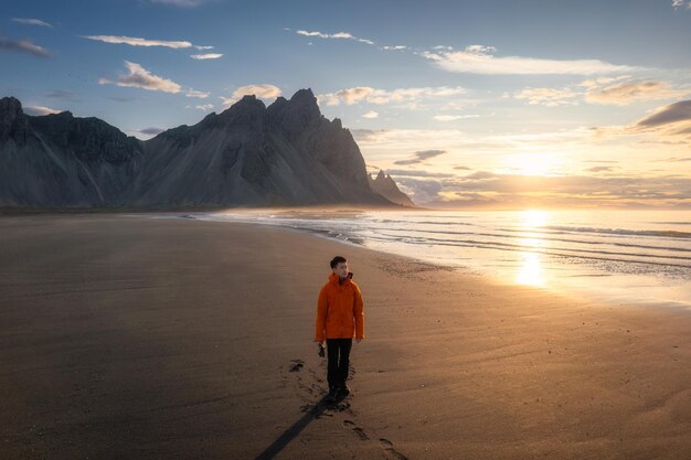 Foto l'alba dorata sulla montagna vestrahorn e l'uomo in piedi sulla spiaggia di sabbia nera durante l'estate nella penisola di stokksnes a icelandla in islanda