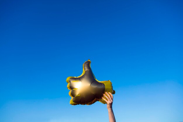 Golden thumbs up like balloons held up against a bright blue summer sky