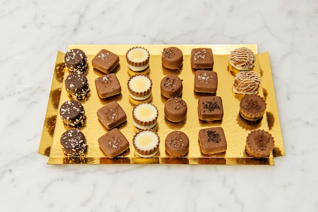 Golden tray with assorted artisan chocolates on white marble table