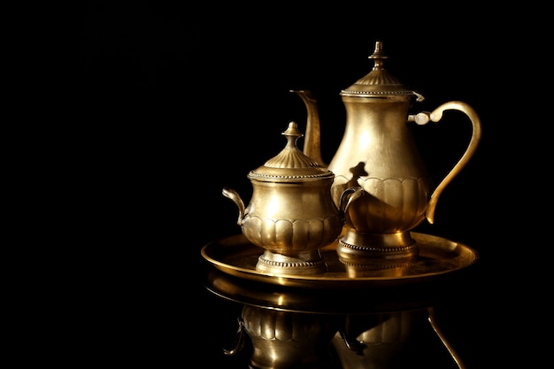 Golden tray with teapot and sugar bowl on black background