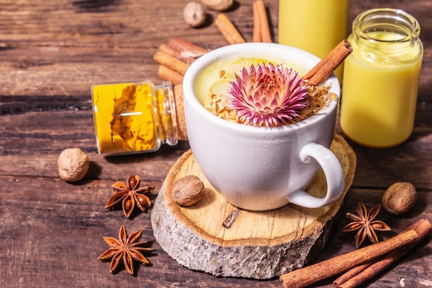 Golden turmeric milk with ice. Cinnamon, nutmeg, anise spices. Healthy morning breakfast drink concept. A modern hard light, dark shadow, old wooden table, close up