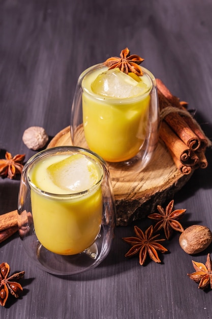 Golden turmeric milk with ice. Cinnamon, nutmeg, anise spices. Trendy healthy drink concept. A modern hard light, dark shadow, black wooden background, copy space