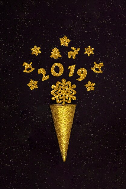 Cono di cialda d'oro con figure 2019 e decorazioni natalizie, fiocchi di neve su fondo nero