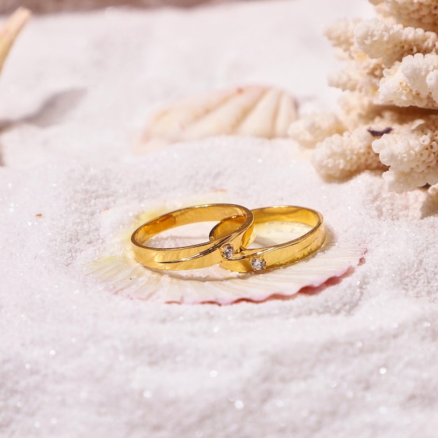 Golden wedding diamond rings lie on sand beach