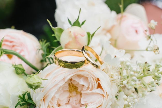 Golden wedding rings and a beautiful wedding bouquet of roses and eustoma in the background closeup