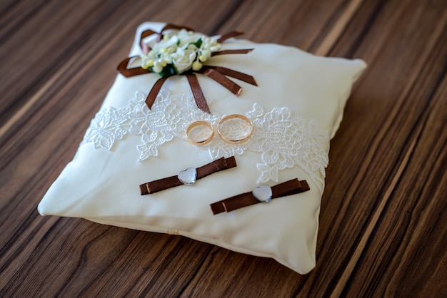 Golden wedding rings on a beautiful white pillow brown ribbons and flowers