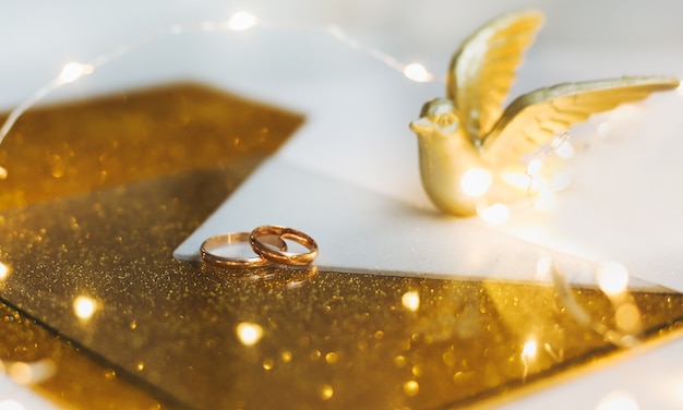 Golden wedding rings on golden background with toy bird and decorations.