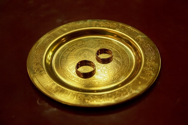 Photo golden wedding rings on a plate in church