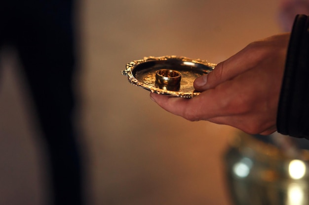 Golden wedding rings on plate in priest hand at traditional ceremony in church