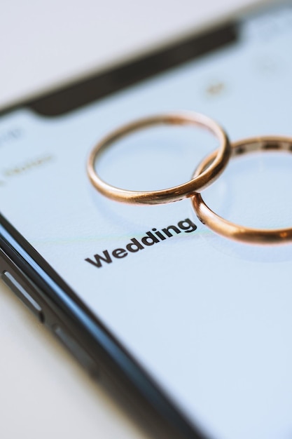 Photo golden wedding rings on top of a smartphone and the text on the screen wedding