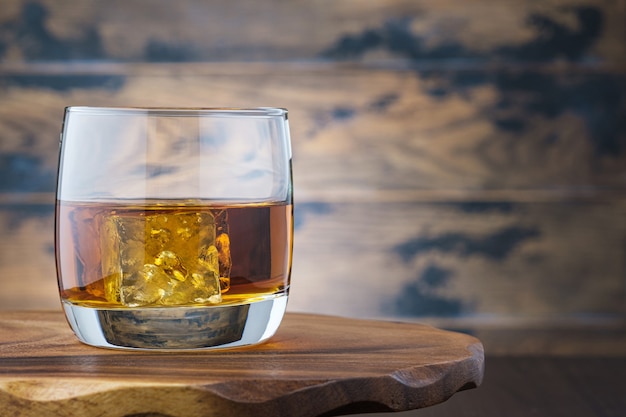 Golden whiskey or bourbon with ice cubes in glass. On wooden table glass with whisky or brandy. Alcohol drink