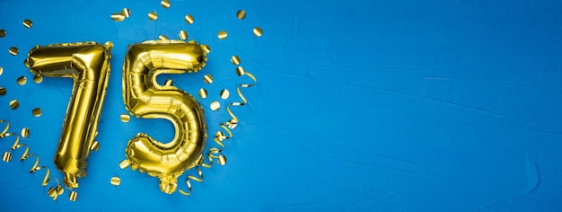 Golden yellow foil balloon on blue concrete background number seventy five birthday or anniversary card with the inscription 75 anniversary celebration