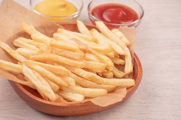 Golden yummy deep French fries on kraft baking sheet paper and serving tray to eat with ketchup and yellow mustard, close up, lifestyle.