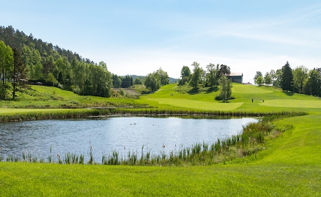 Поле для гольфа с прудом, голубым небом и зеленой природой