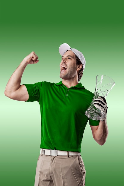 Foto giocatore di golf in una camicia verde che celebra con un trofeo di vetro nelle sue mani, su uno sfondo verde.