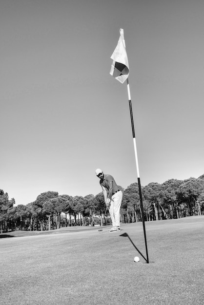 Foto giocatore di golf che colpisce il colpo con il club in corso alla bella mattina con il chiarore del sole sullo sfondo in bianco e nero