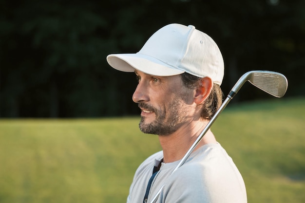 Golf player posing with golf club. training of handsome mature\
man on green sunny course.