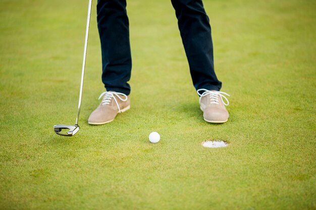 Golfbal, putter en benen van de jongen op groen