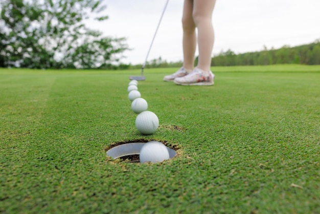 Giocatore di golf donna asiatica sportiva che mette la pallina da golf nel buco magnificamente sulla doppia esposizione di golf verde