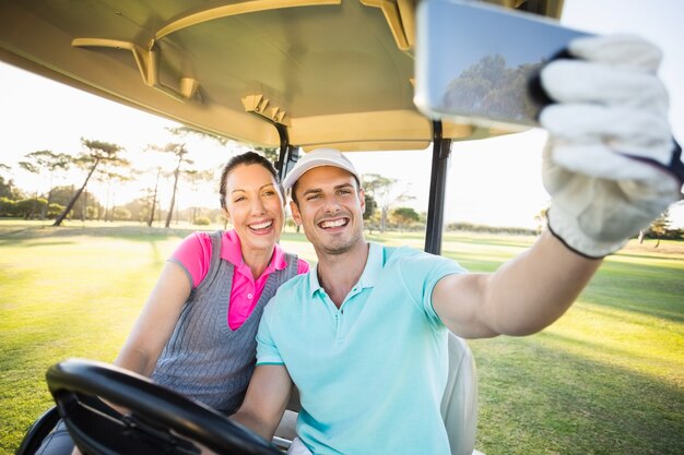 Golfer couple taking selfie while sitting in golf buggy