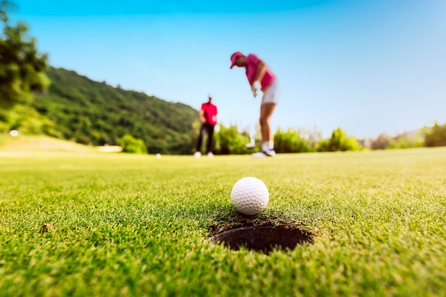 照片高尔夫球手集中在日落把高尔夫球进洞里,健康和生活方式的概念。