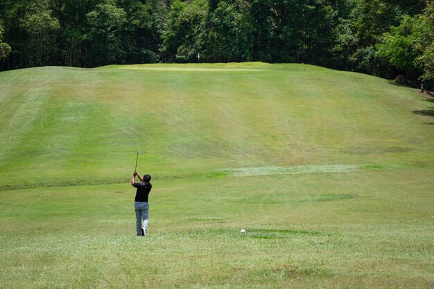 Palla da golf dell'oscillazione del giocatore di golf da forare su bello tratto navigabile e disposizione verdi sul fondo della foresta