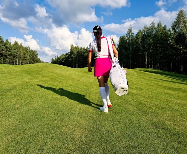 Golfer with bag walks along golf course with back